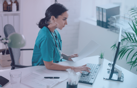 Woman sitting at desk with sheets of paper spread around and is inputting data on a laptop computer